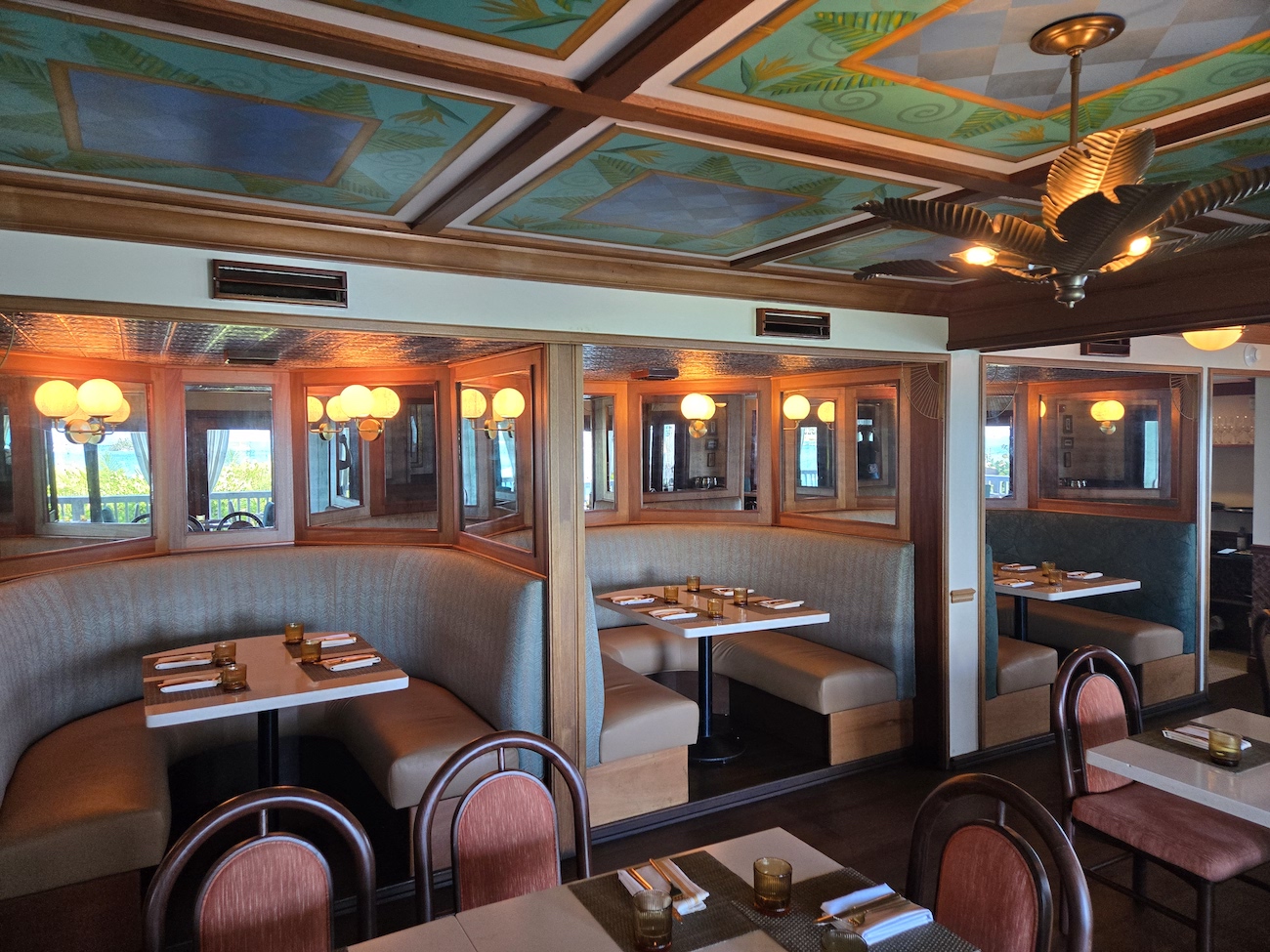Restaurant interior with curved booth seating, wooden tables set for dining, warm lighting, and decorative ceiling panels.