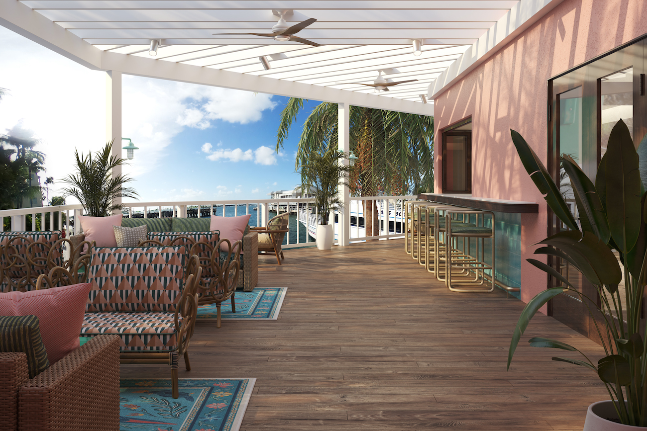 Outdoor patio with wicker seating, patterned cushions, a bar with stools, ceiling fans, wooden floor, and tropical plants under a white pergola overlooking the ocean.