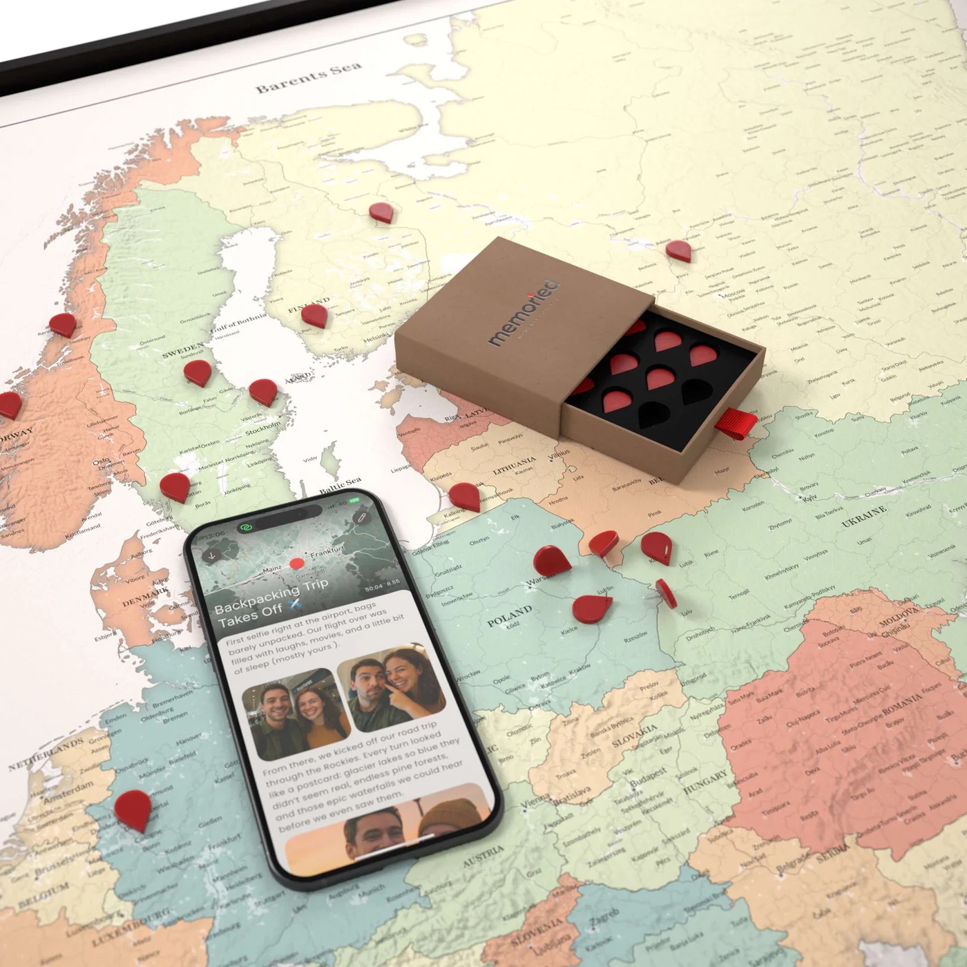 A smartphone, an open box of heart-shaped tokens, and scattered red markers are placed on a map of Europe.