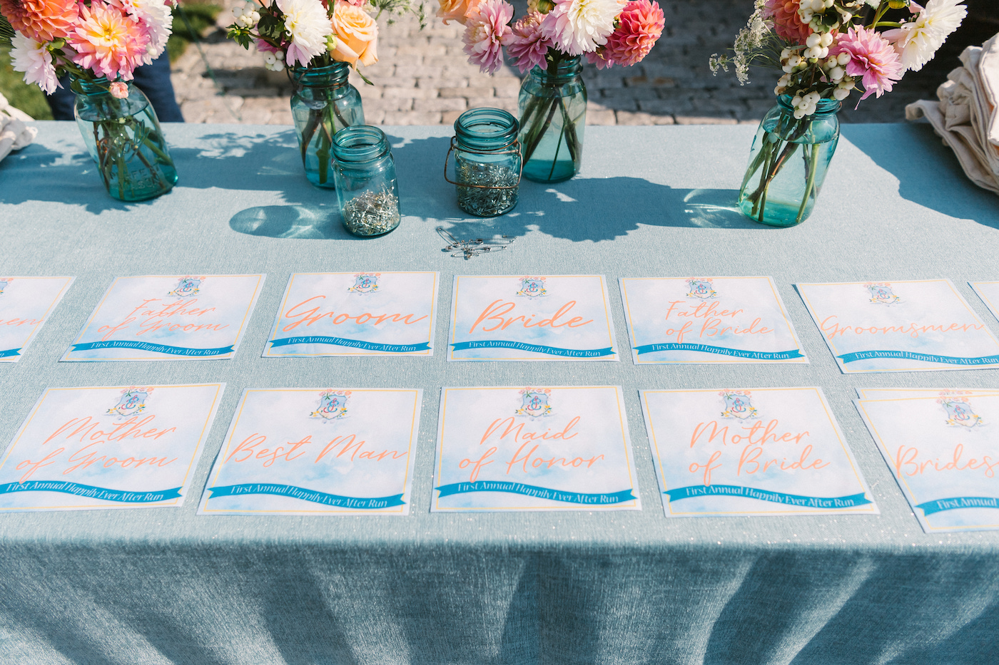 A table displays several name cards in rows, with flower arrangements in blue glass jars placed at the back.