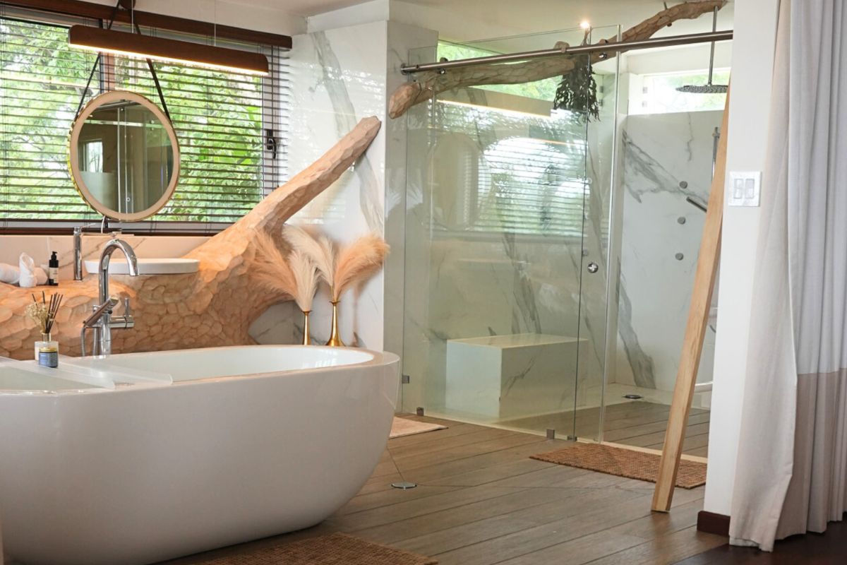 Modern bathroom with a freestanding bathtub, glass-enclosed shower, round mirror, wooden accents, and large windows with blinds.