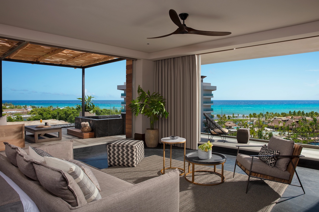 Modern living room at the all-inclusive Mexico resort, Impressions by Secrets Moxché. The photo shows an open patio, neutral furnishings, and panoramic ocean view under a clear blue sky.