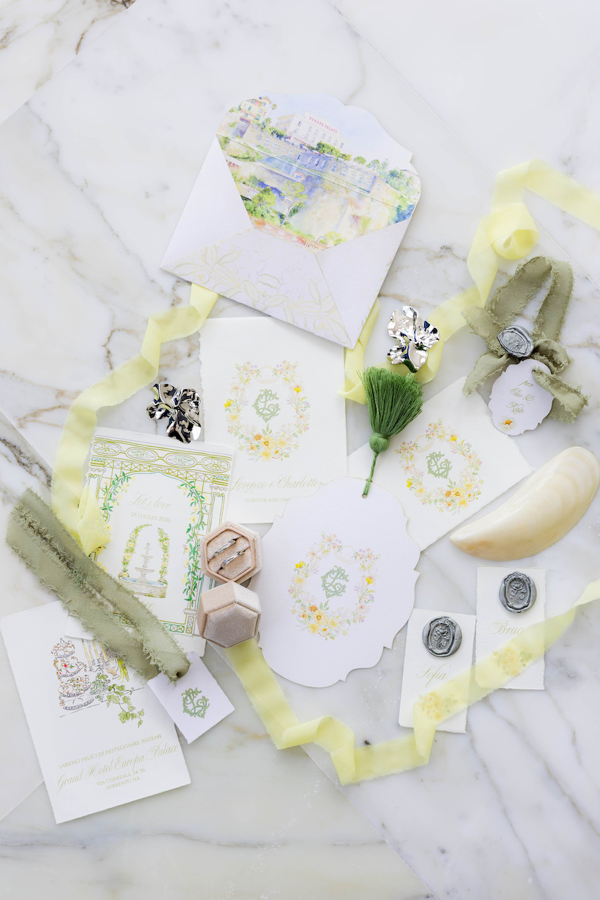 Flat lay of wedding stationery, envelopes, wax seals, ribbon, and decorative items arranged on a marble surface.