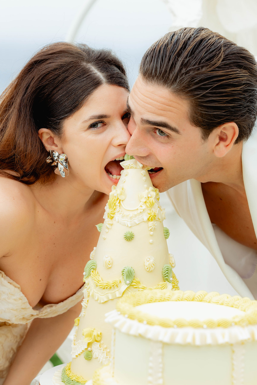 A woman and a man lean in together to take a bite out of the top of a decorated wedding cake.