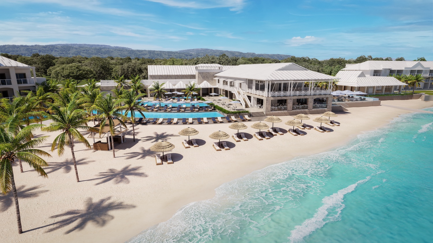 A beachfront resort with white buildings, a swimming pool, palm trees, beach umbrellas, and clear blue ocean under a sunny sky.