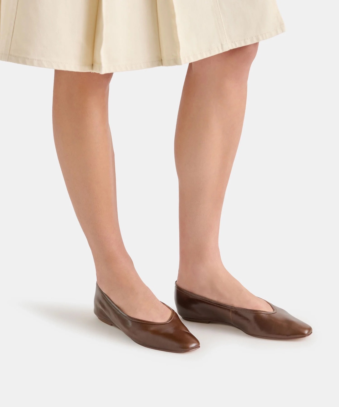 Person wearing a cream skirt and brown pointed-toe flats, standing on a light surface.