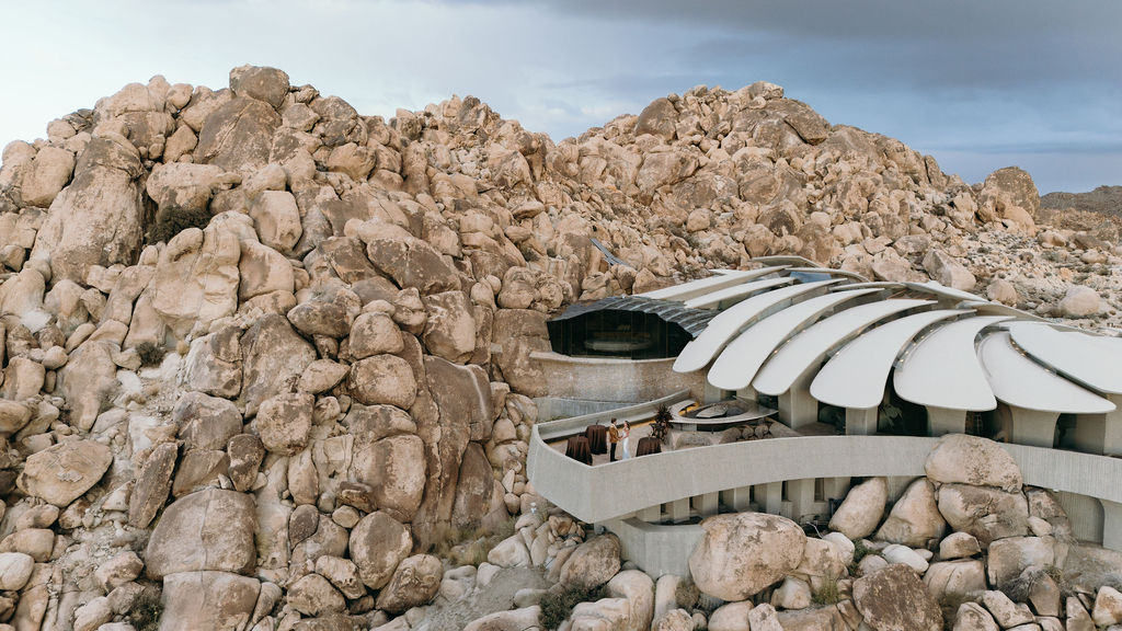 Modern building with a curved white roof is partially embedded among large rocky boulders in a desert landscape.