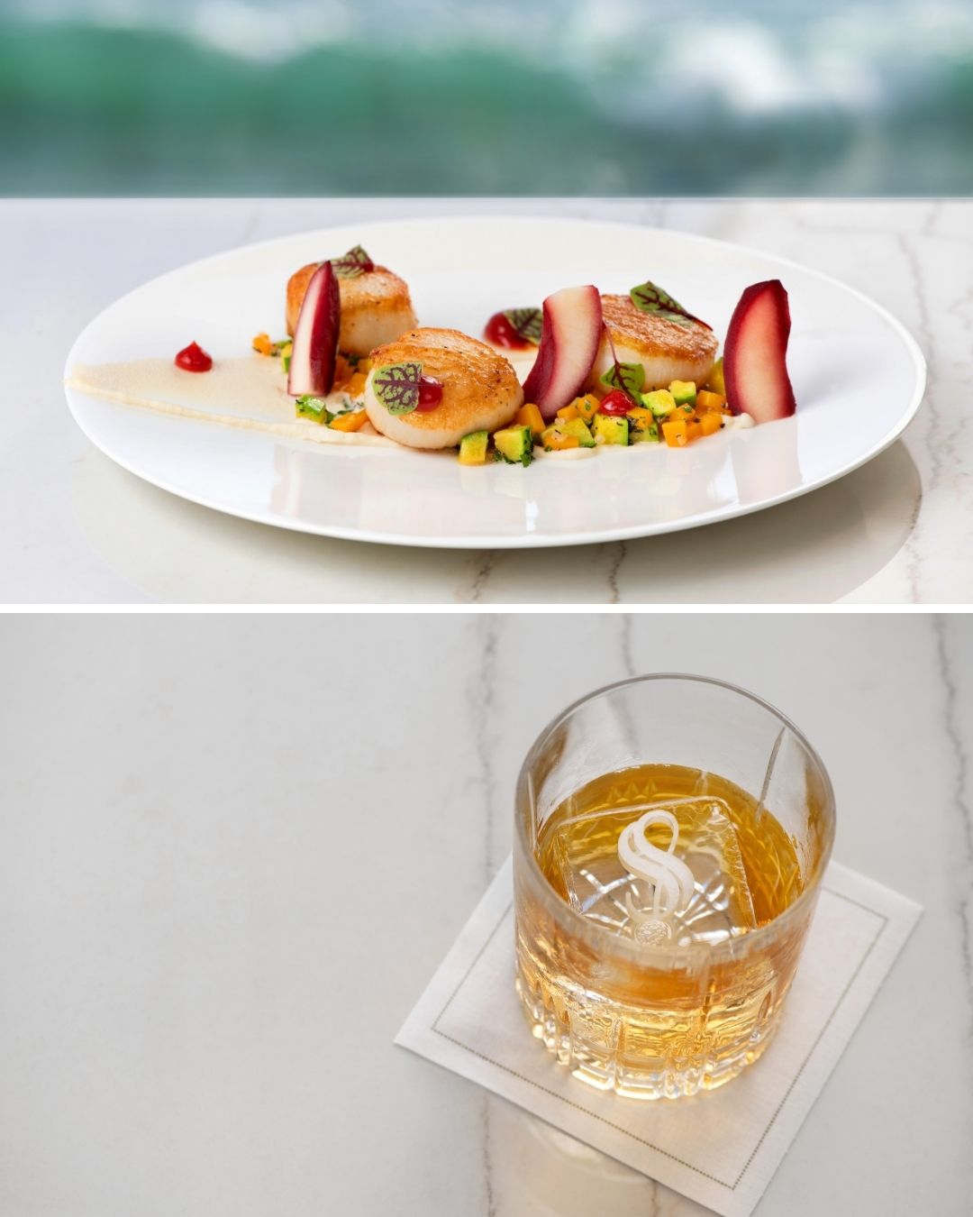 A white plate with seared scallops, vegetables, and garnishes above a glass of amber-colored whiskey on a marble surface.