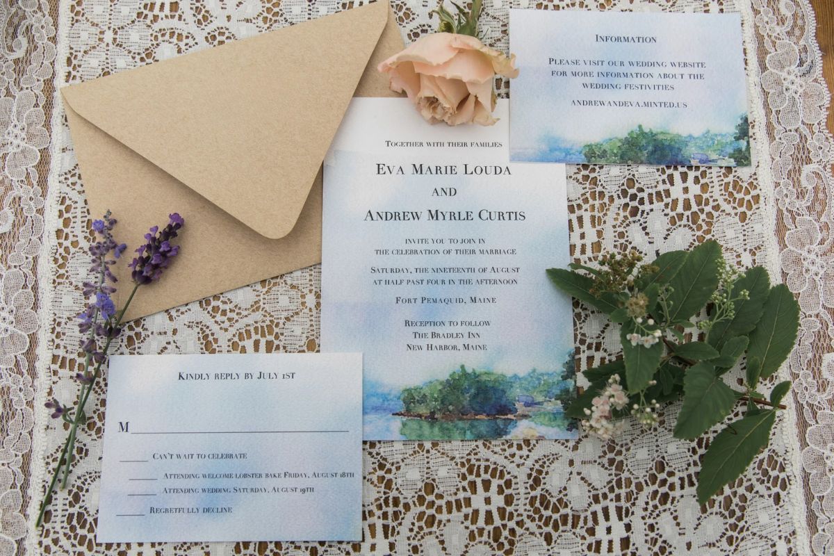 A wedding invitation suite with envelopes, RSVP card, and floral decorations arranged on a lace tablecloth.