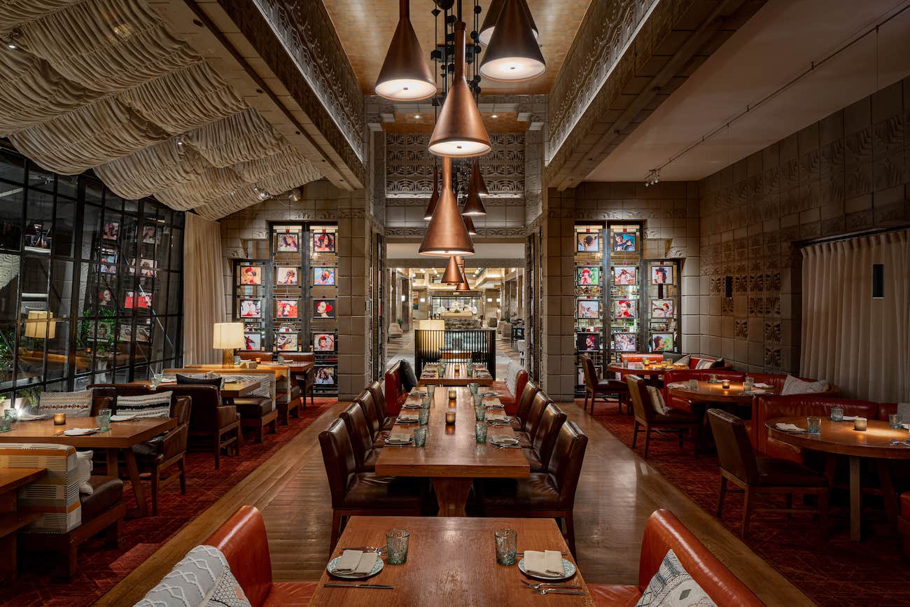 Modern restaurant interior with wooden tables, leather chairs, decorative lighting, and artistic wall displays, set for dining.