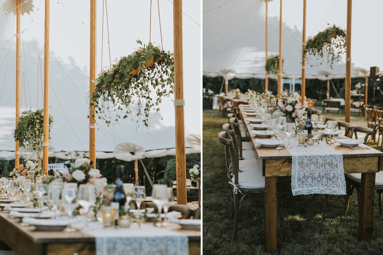 Long wooden tables with lace runners, floral centerpieces, and hanging greenery are set up outdoors under a white tent for an event.