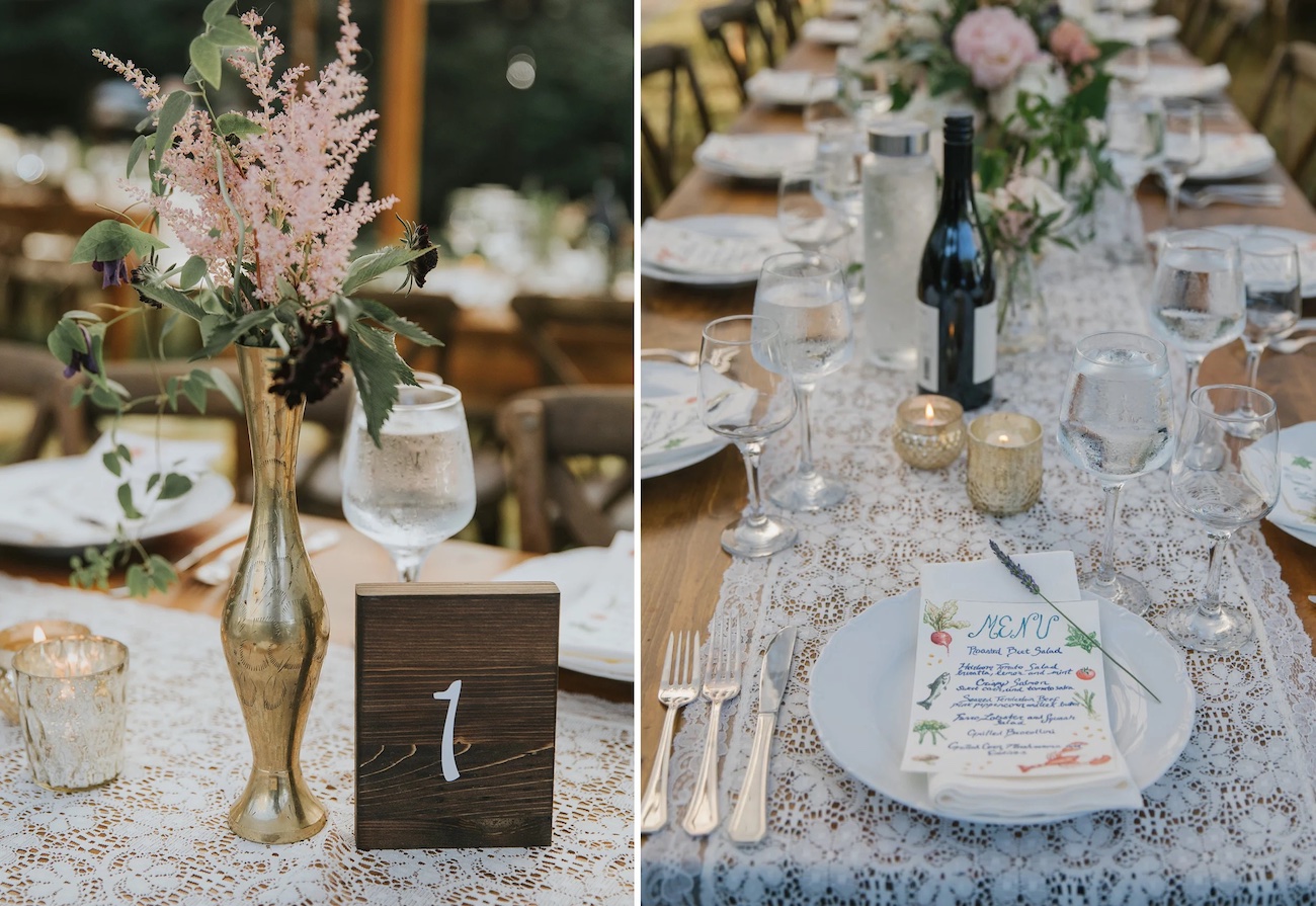 A wedding table setting with floral centerpieces, tableware, candles, wine, and a wooden table number on a lace table runner.