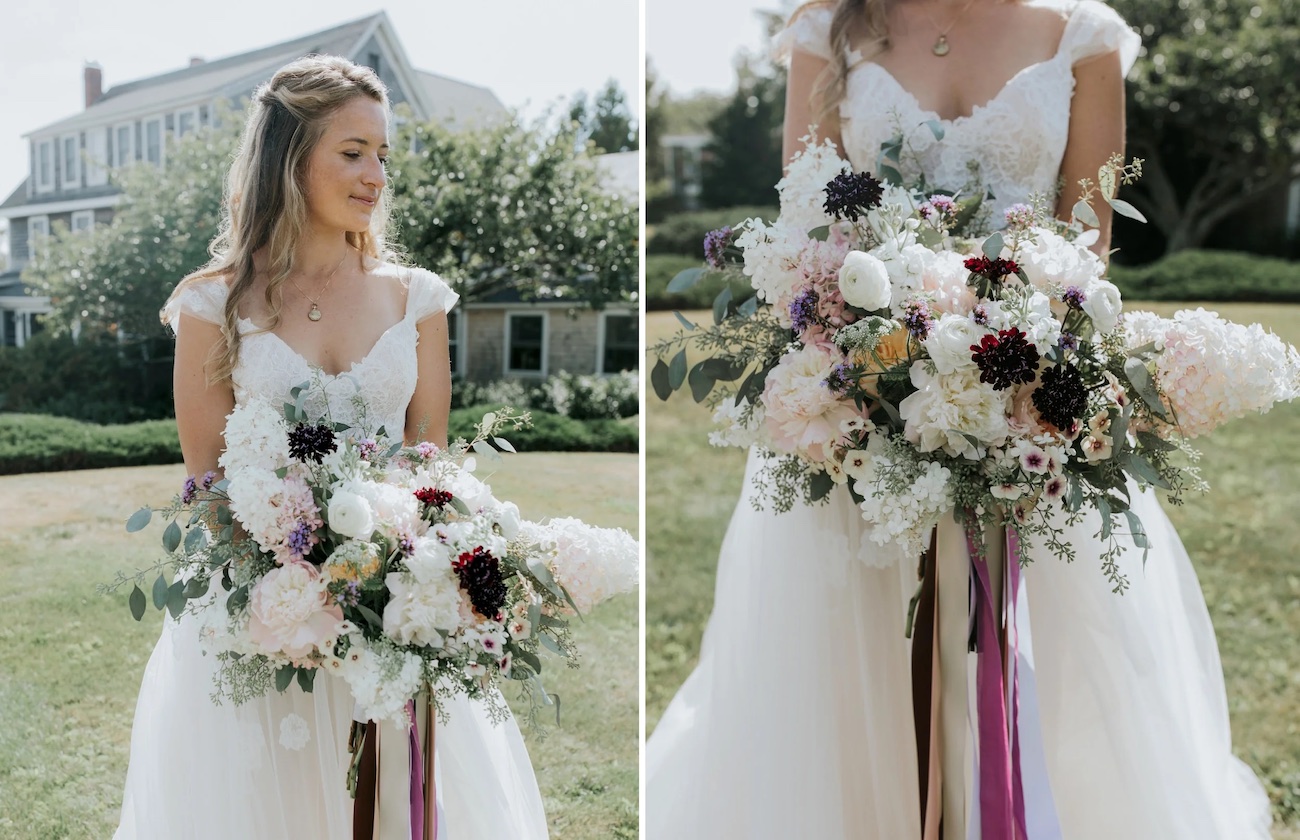 A bride in a white dress holds a large bouquet of assorted flowers outdoors, with a house and greenery in the background.