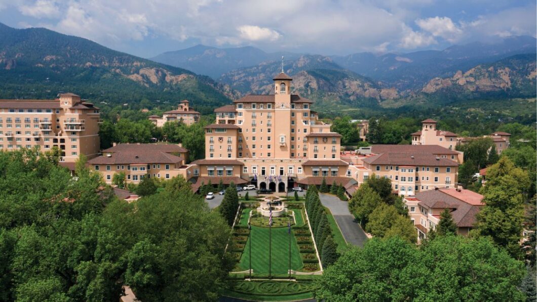 Aerial view of The Broadmoor resort complex featuring several large buildings, landscaped gardens, and mountains in the background.