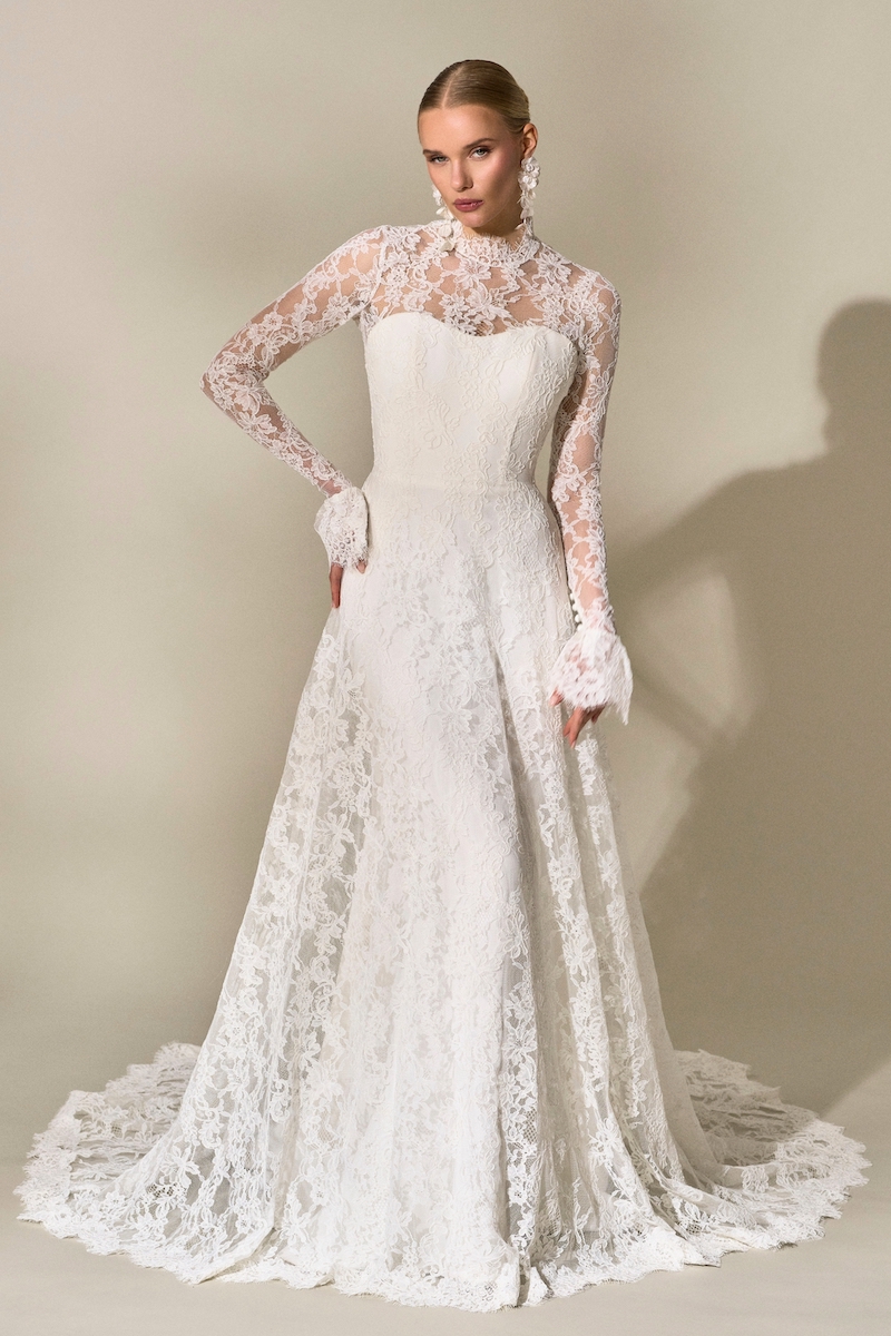 A floor-length white lace wedding dress with a high neckline, long sleeves, and a train.