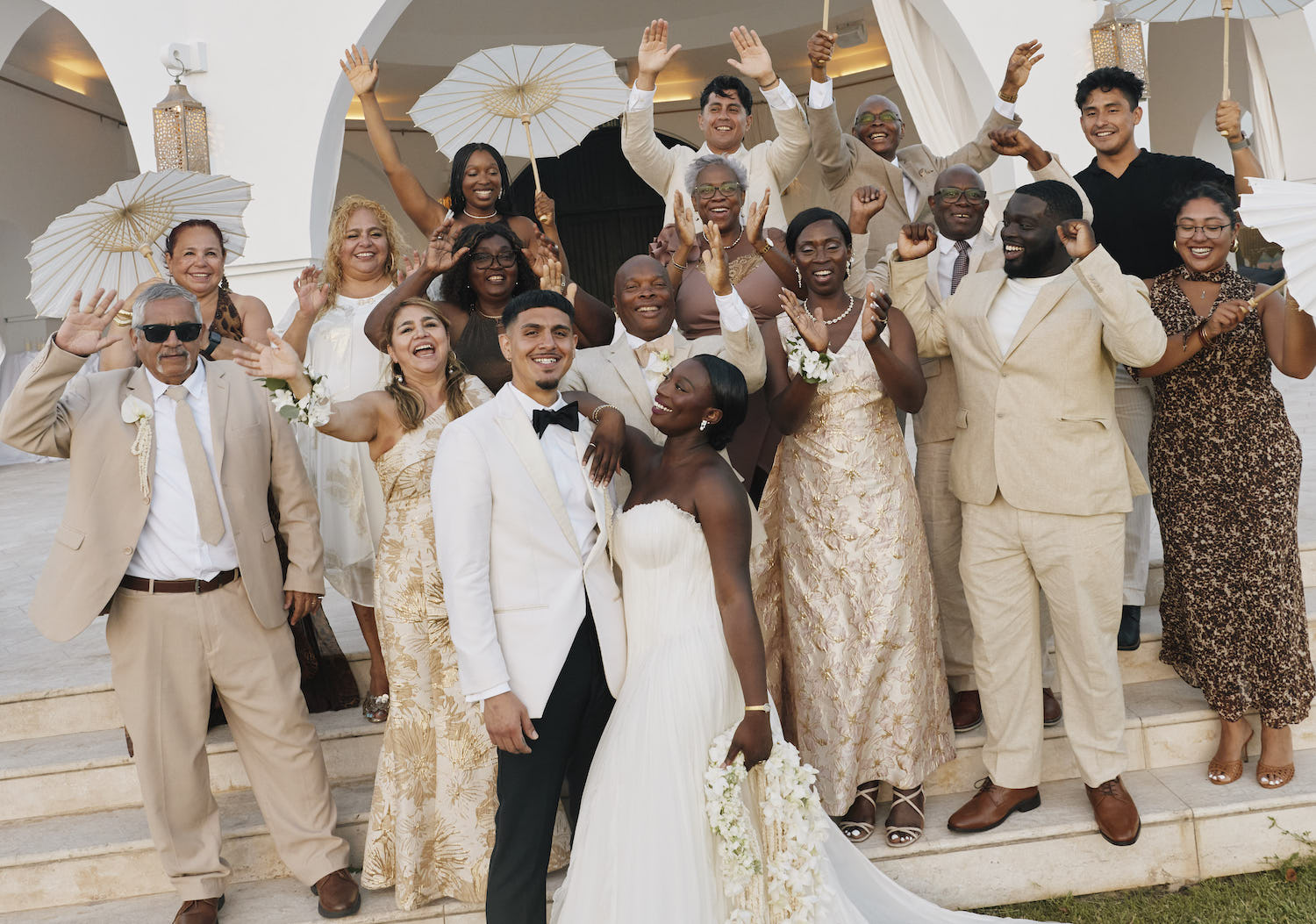A bride and groom surrounded by their wedding party on steps in front of a white building.