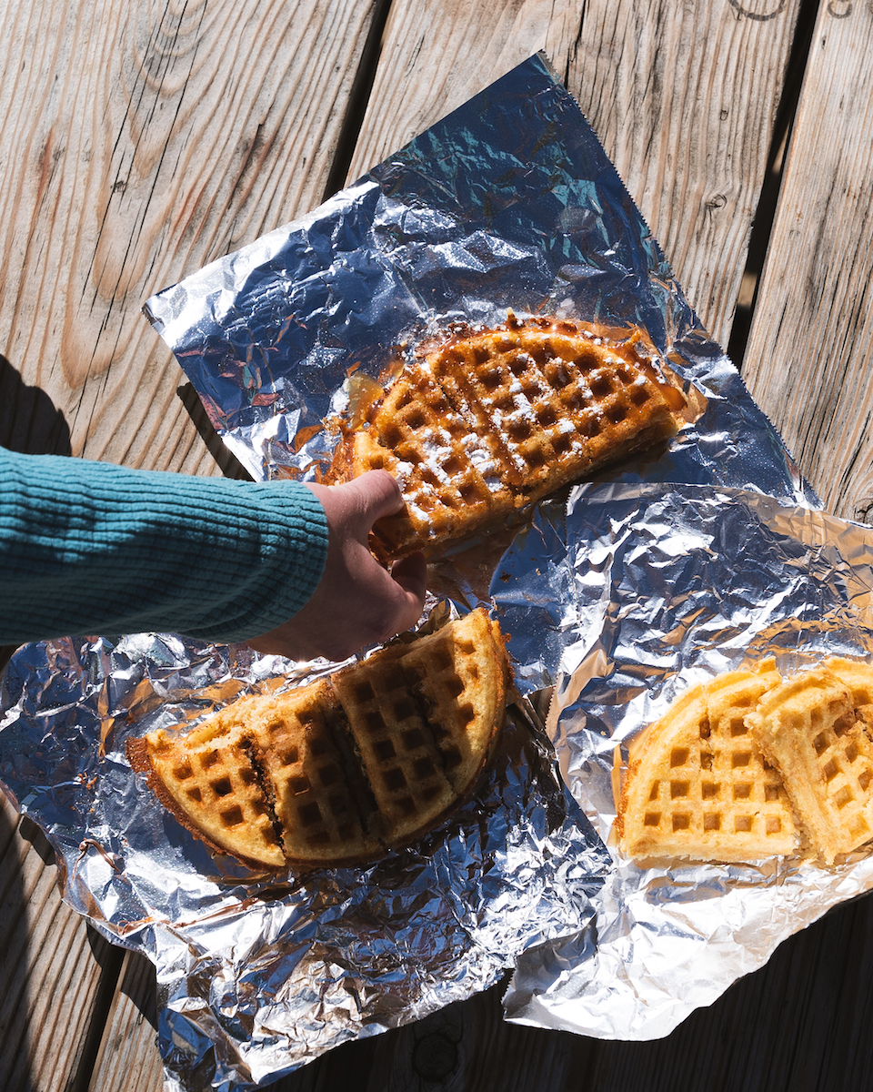 A hand reaching for a piece of waffle on aluminum foil.