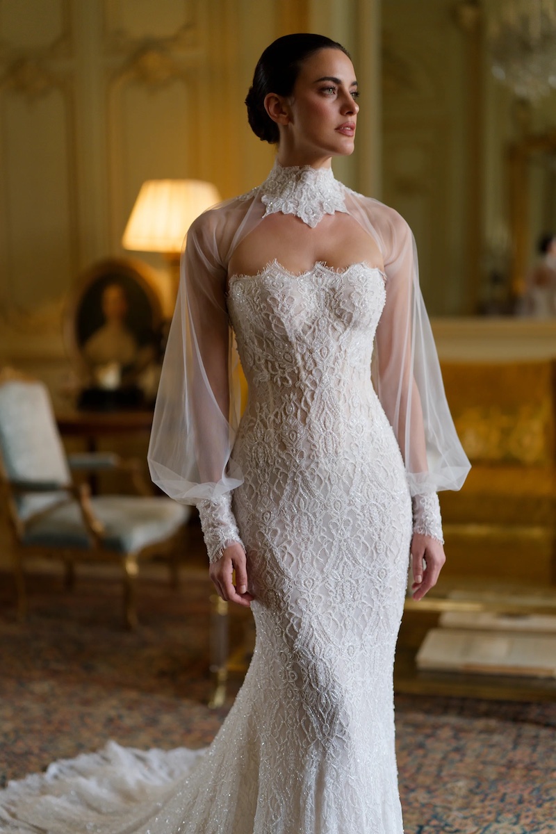 A woman wearing a lace mermaid-style wedding dress with a sheer high-neck overlay and long bishop sleeves.