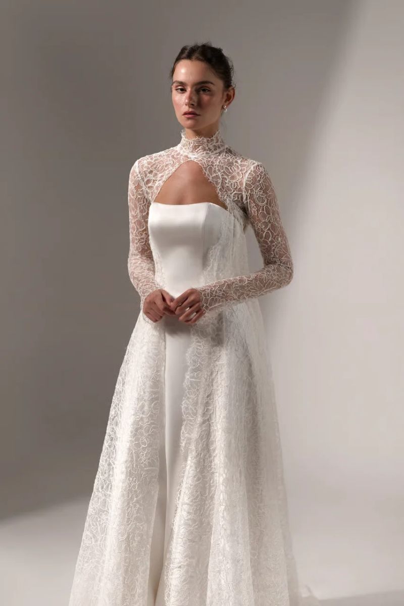 A white wedding dress with a strapless bodice and a high-neck, long-sleeved lace overlay.