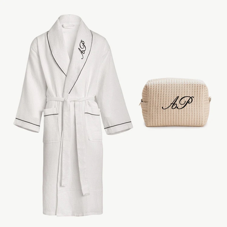 White robe with black piping and an “AP” monogram, paired with a matching beige zippered pouch embroidered with “AP.”