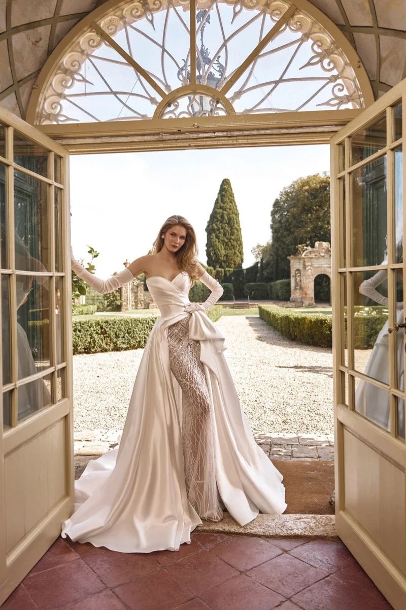 A person in an off-the-shoulder wedding gown with dramatic skirt standing in an arched doorway.