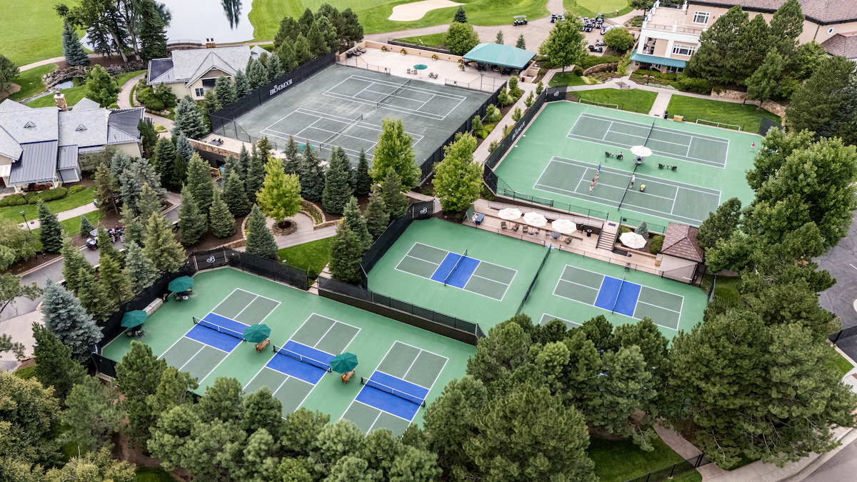 Aerial view of a tennis complex with several courts nestled among trees and buildings.