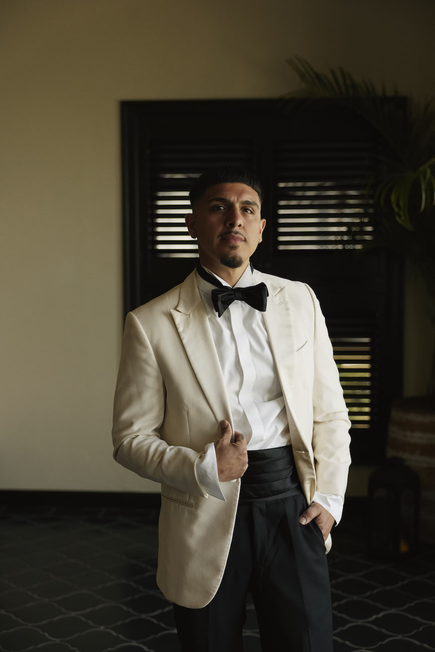 A man wearing a white dinner jacket, black bowtie, and black tuxedo trousers.