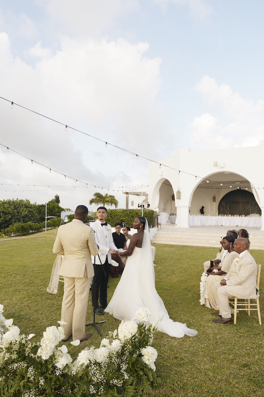 A couple exchanges wedding vows during an outdoor ceremony, standing before an officiant with seated guests nearby.