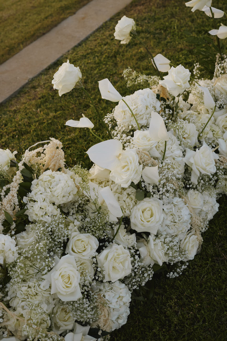 Large arrangement of white roses and baby’s breath on a patch of grass.
