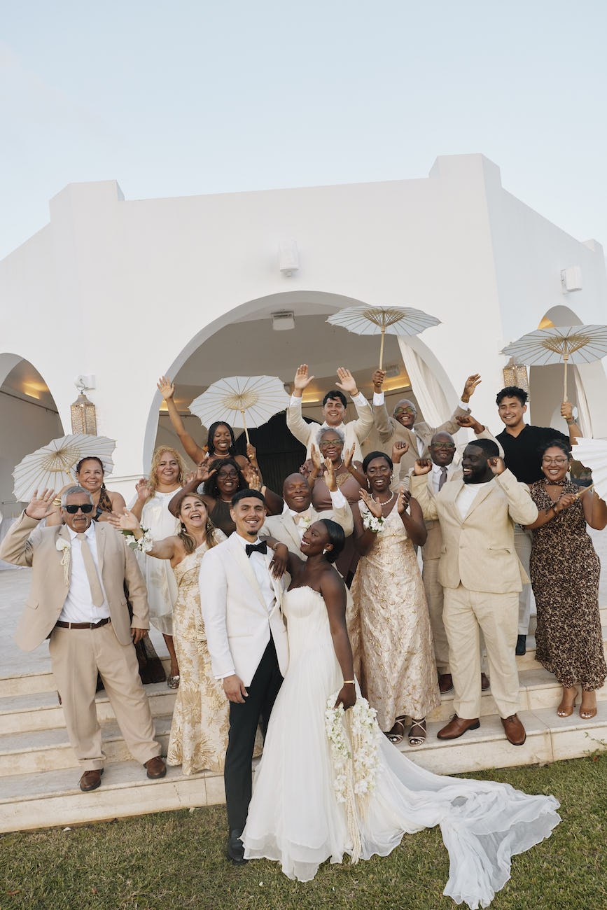 A newlywed couple posing with a large group of wedding guests in front of a white building.