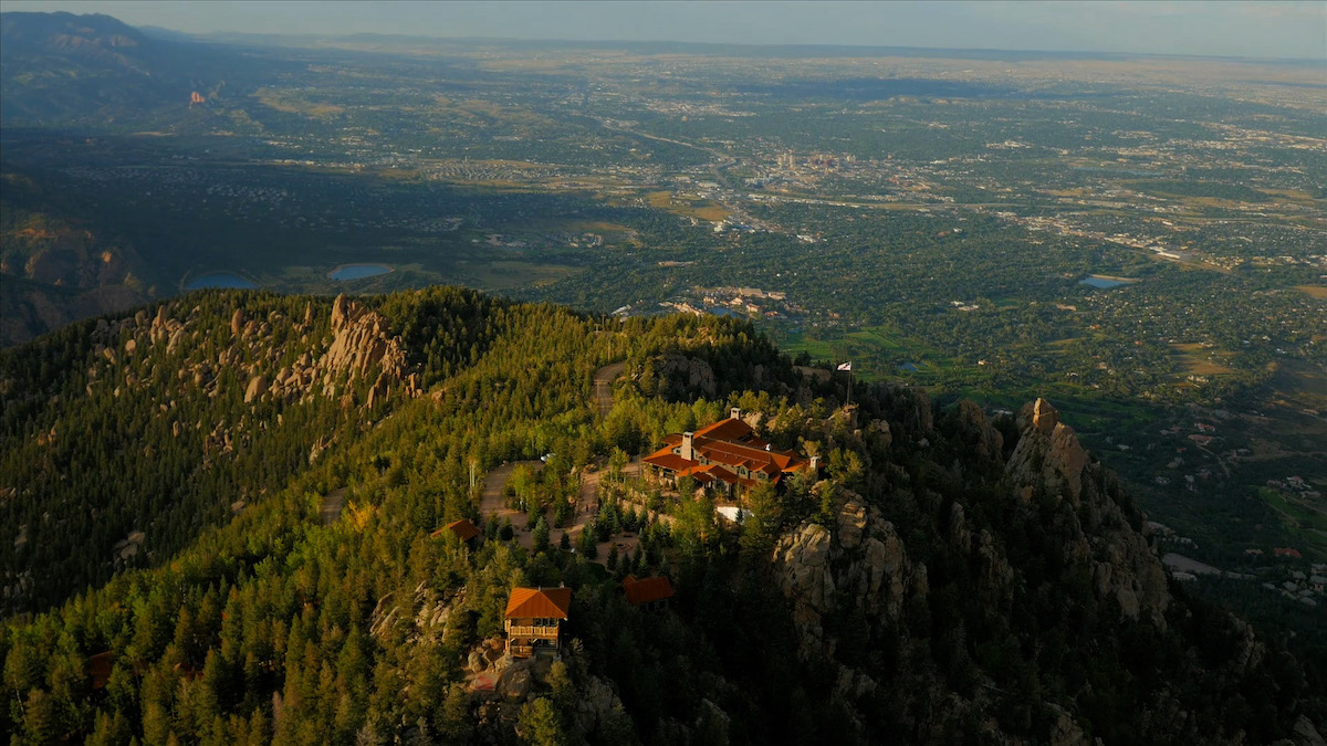 Aerial view of buildings nestled on a forested mountain ridge overlooking a valley.