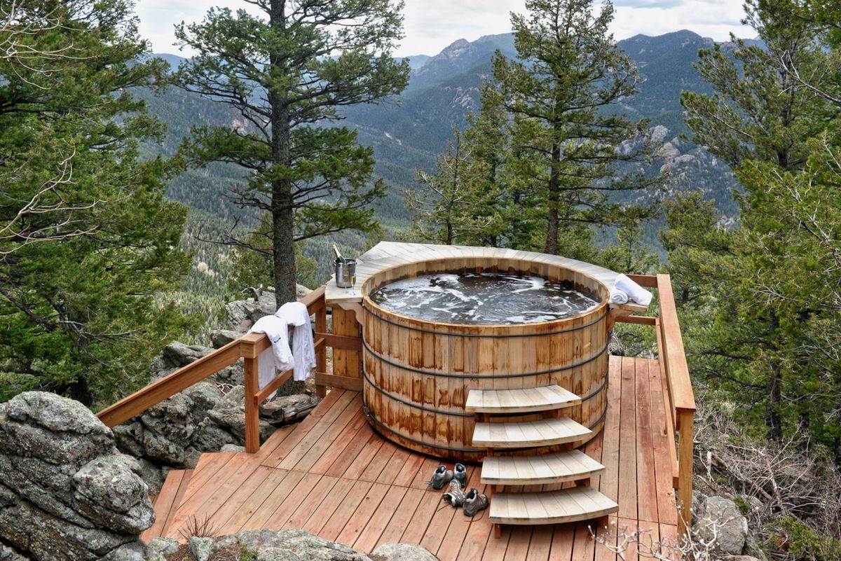 A round wooden hot tub on a deck overlooking a mountainous forest.