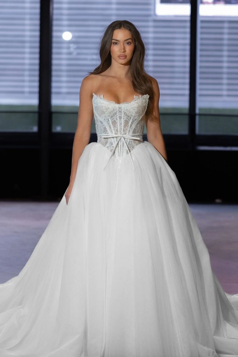 A model wearing a white, strapless ballgown with a corset bodice and a full tulle skirt on a runway.