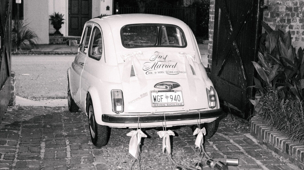 A small vintage car decorated with “Just Married” signage and tin cans trailing from the rear bumper.