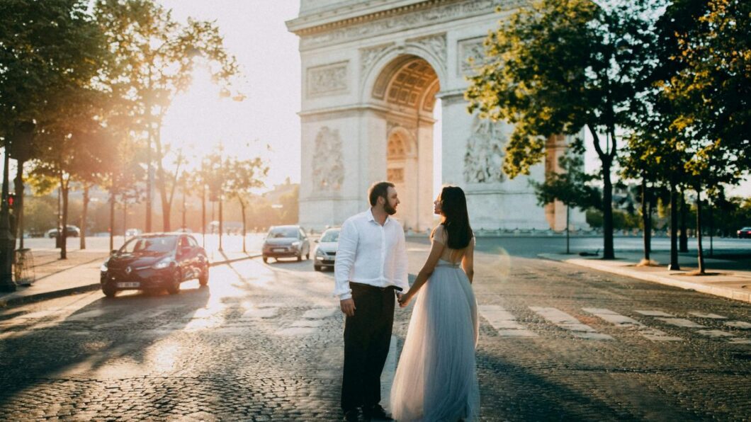 A couple holding hands while standing in front of the Arc de Triomphe in Paris.