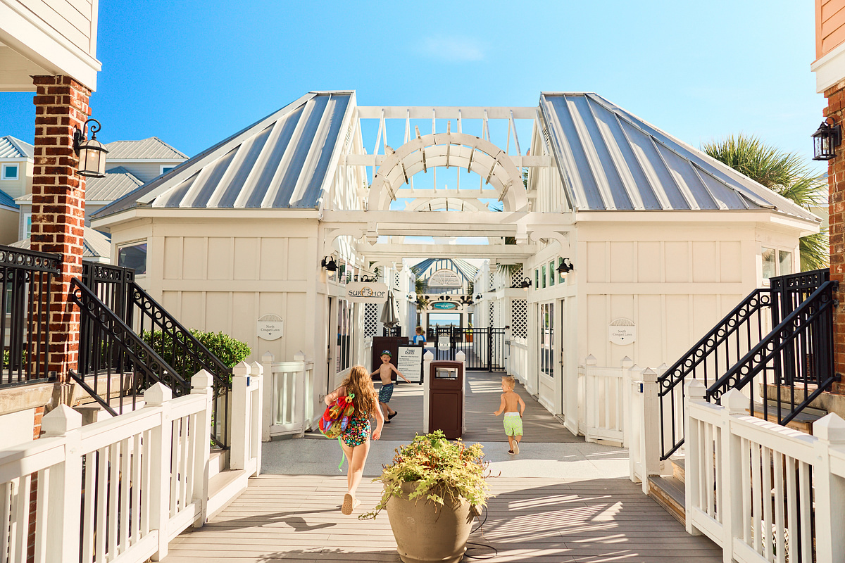 Two children running through a white wooden corridor leading to a boardwalk area.