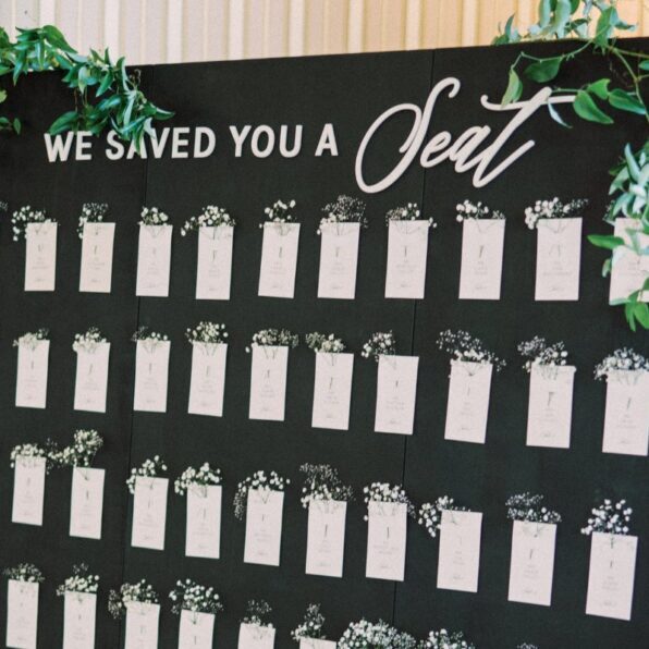 "We saved you a seat" black sign with seating chart and greenery