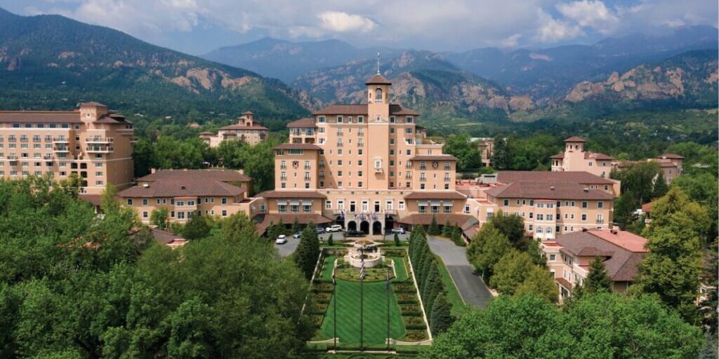 Aerial view of The Broadmoor resort complex featuring several large buildings, landscaped gardens, and mountains in the background.