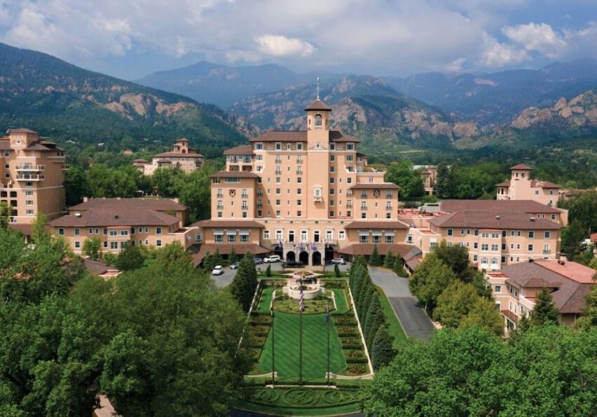 Aerial view of The Broadmoor resort complex featuring several large buildings, landscaped gardens, and mountains in the background.