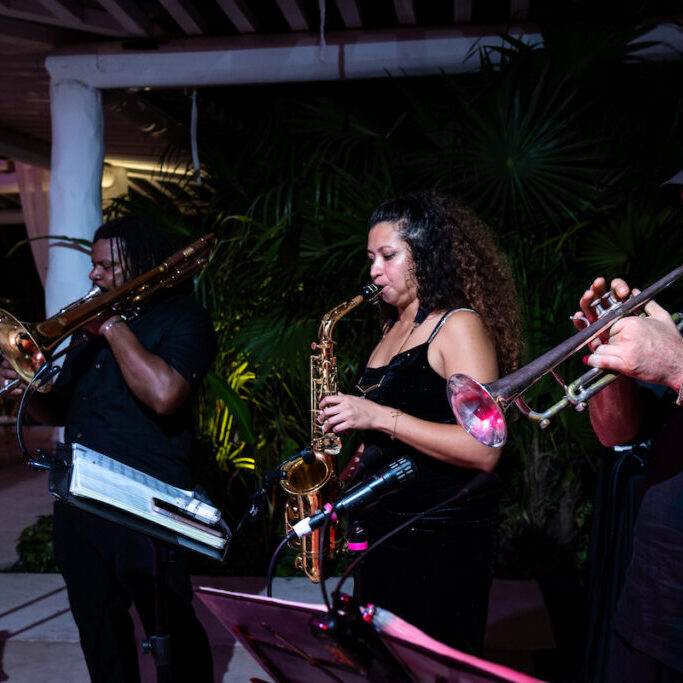 Three musicians perform on brass instruments outdoors at night.