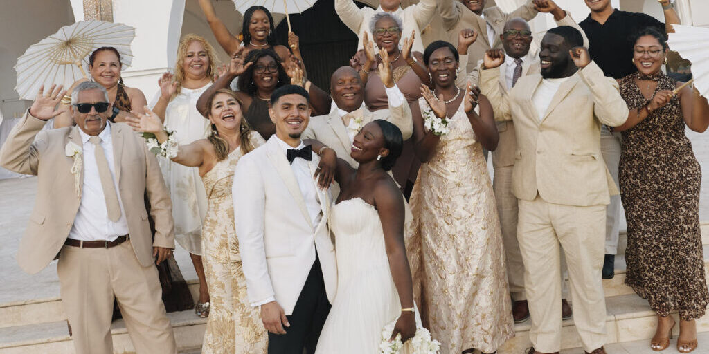 A bride and groom surrounded by their wedding party on steps in front of a white building.