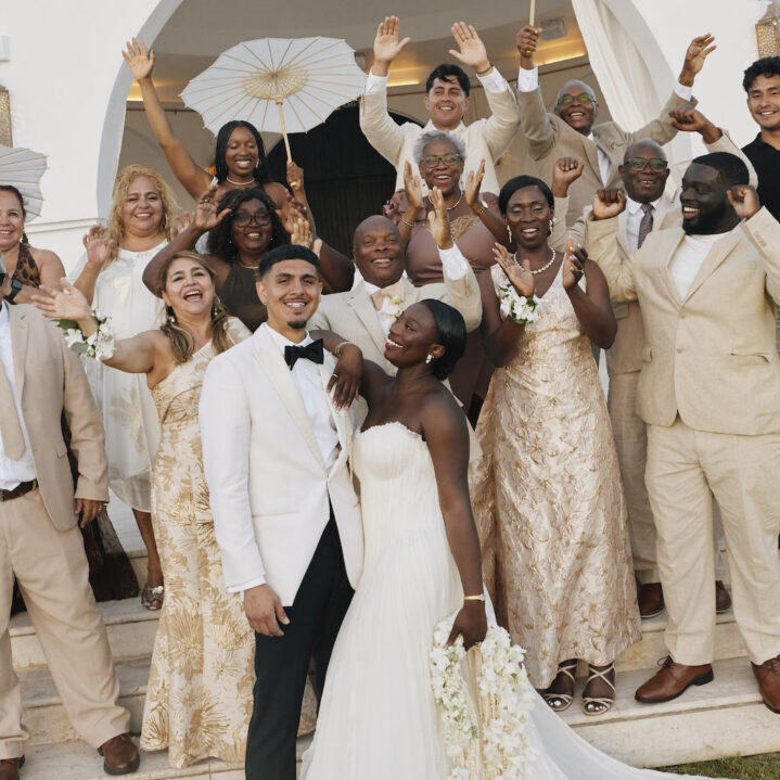 A bride and groom surrounded by their wedding party on steps in front of a white building.