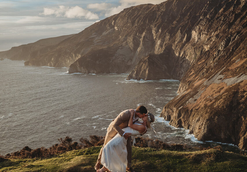 A bride and groom kiss romantically during their elopement on the cliffside in Ireland