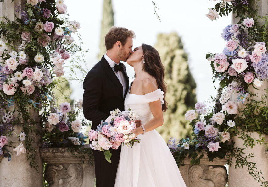 Wedding couple kissing among ceremony arch and flowers
