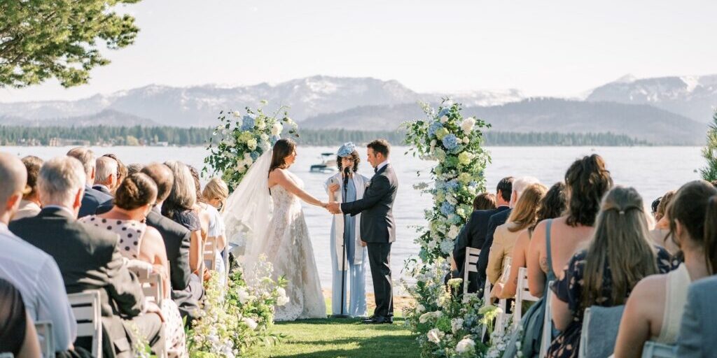 A bride and groom share a moment on the shores of Lake Tahoe with the mountains and blue water in the background.