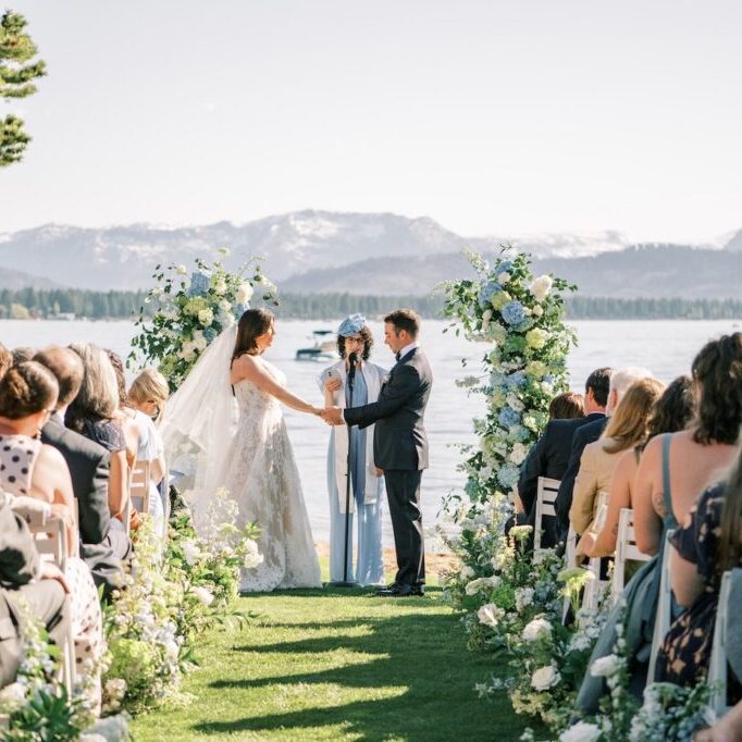 A bride and groom share a moment on the shores of Lake Tahoe with the mountains and blue water in the background.