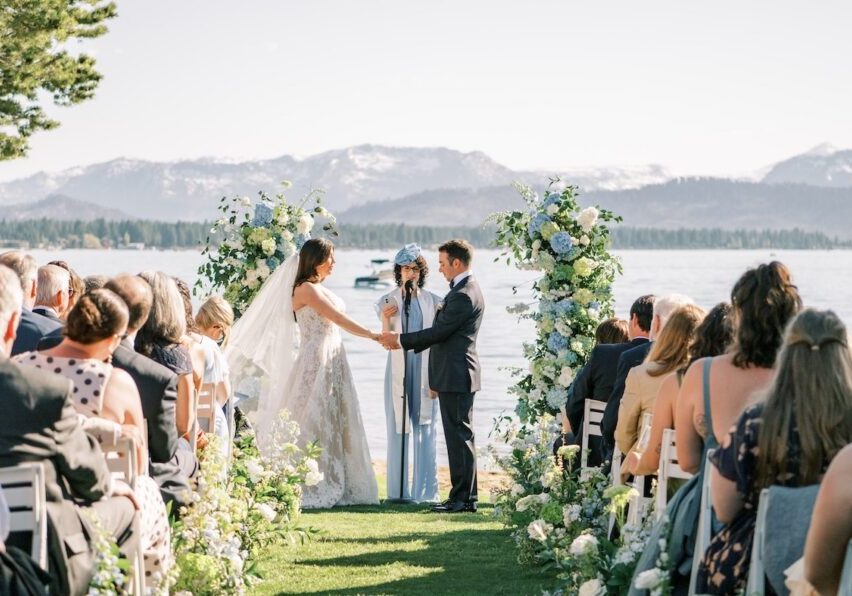 A bride and groom share a moment on the shores of Lake Tahoe with the mountains and blue water in the background.