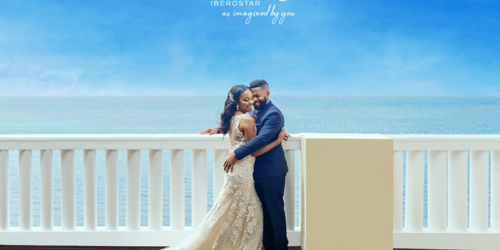 bride and groom hug on terrace overlooking the Caribbean Sea with the Iberostar Weddings logo