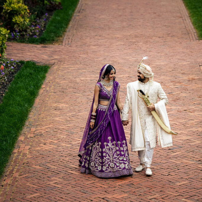 couple in Indian wedding attire walk hand in hand on brick pathway of the Biltmore Estate