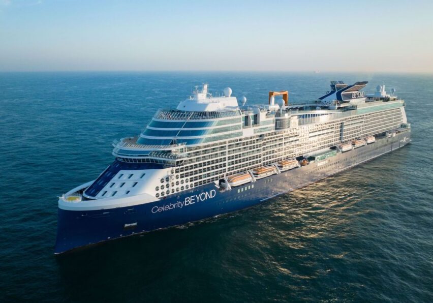 A large blue and white cruise ship sails on calm ocean waters under a clear sky.